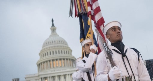 Sailors march holding flags with the U.S. Capitol building in the background.